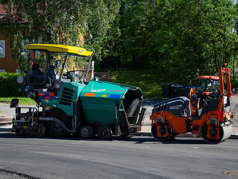 Vibroacabadora e rolo compactador aplicando asfalto em uma rua