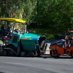 Vibroacabadora e rolo compactador aplicando asfalto em uma rua